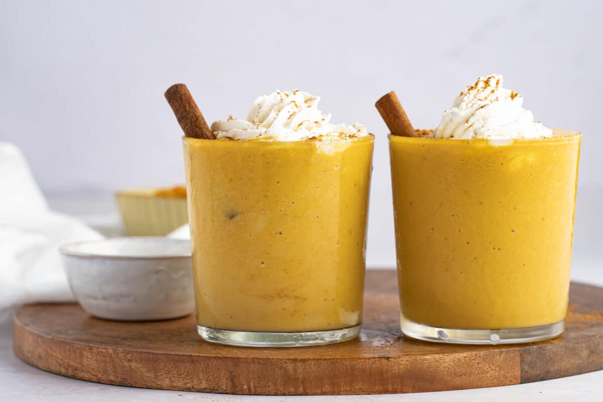 pumpkin spice smoothies in clear glasses with cinnamon sticks and whipped cream