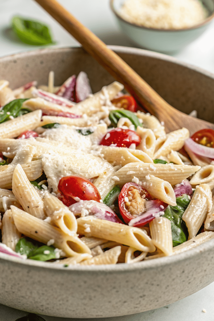 Close up image of pasta salad in a large bowl before it's been mixed well.