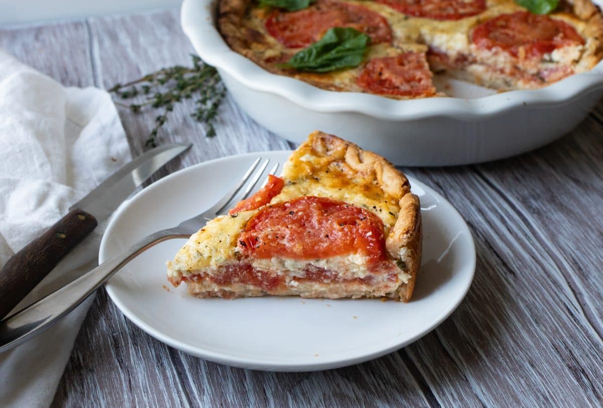 a slice of fresh tomato pie on a white plate with a fork