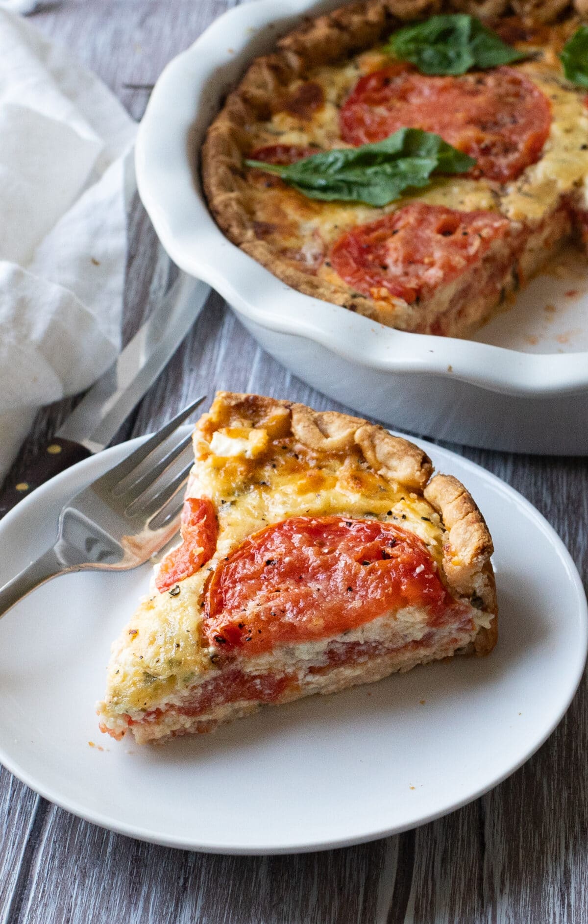 slice of tomato pie with mozzarella cheese on a white plate with the rest of the pie in the background