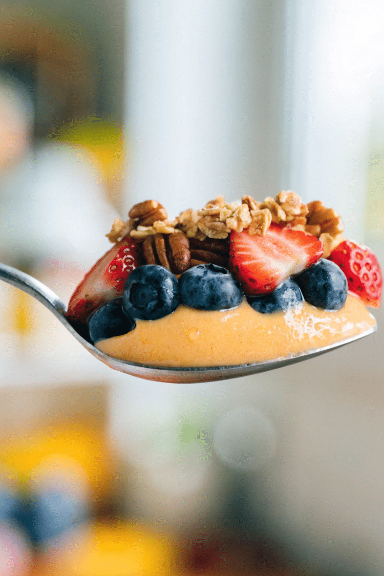 close up of mango smoothie with fruit and granola on a spoon