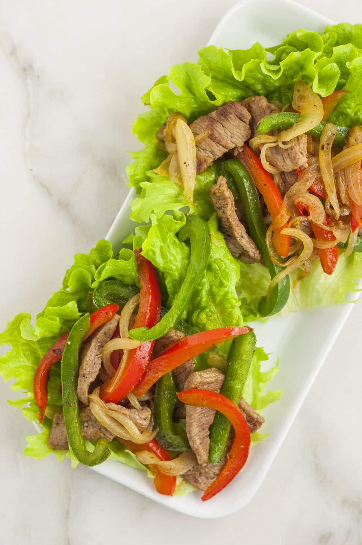 two philly cheesesteak lettuce wraps on a white plate on a marble countertop