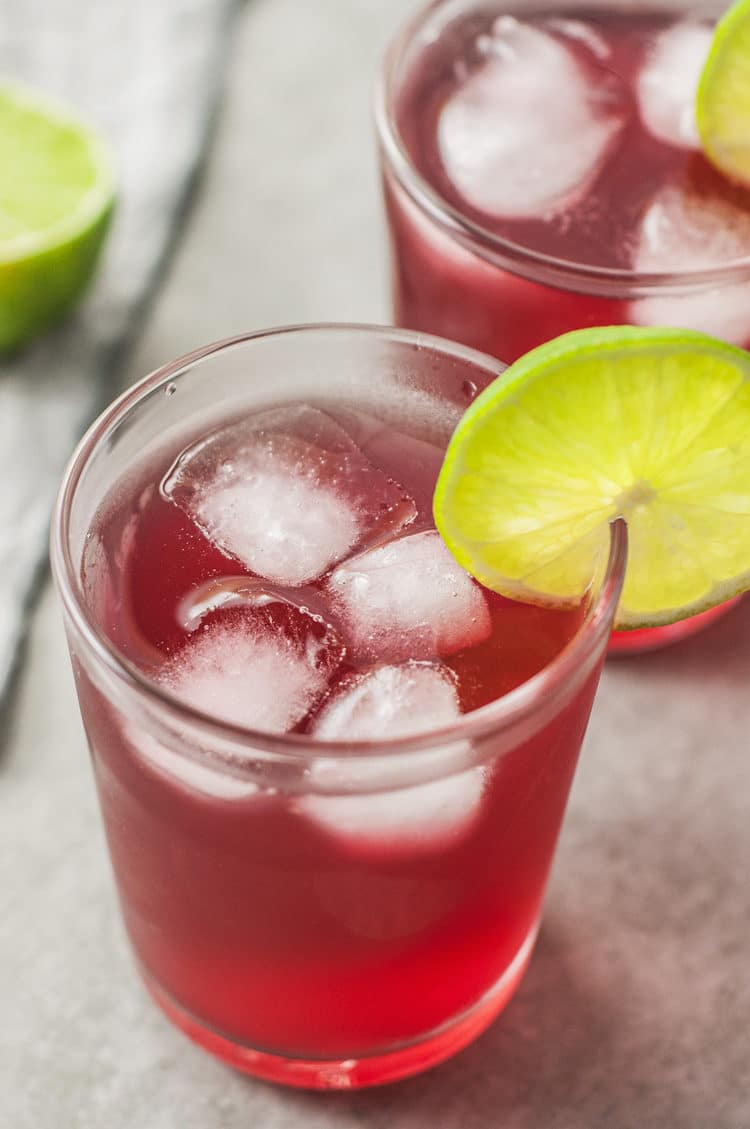 close up of apple cider vinegar and cranberry detox drink with ice cubes and a lime slice