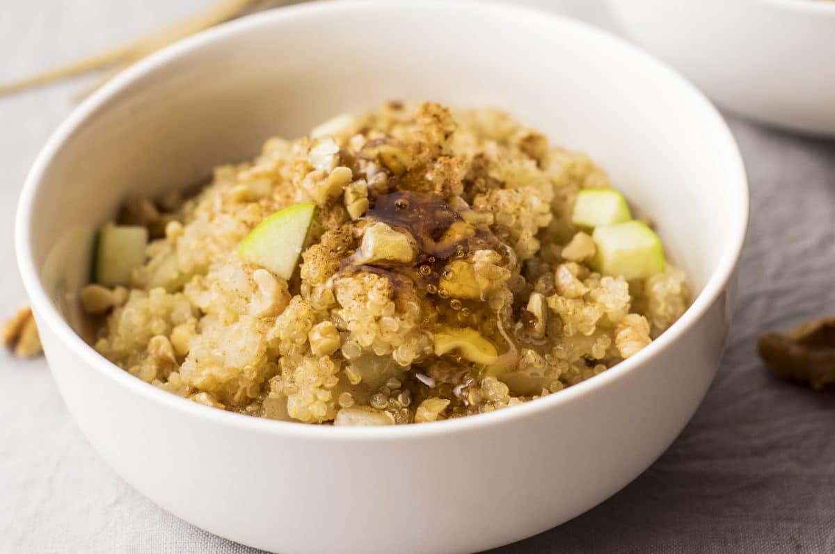 Upper side view of quinoa and apple recipe in a white serving bowl that's been drizzled with maple syrup.
