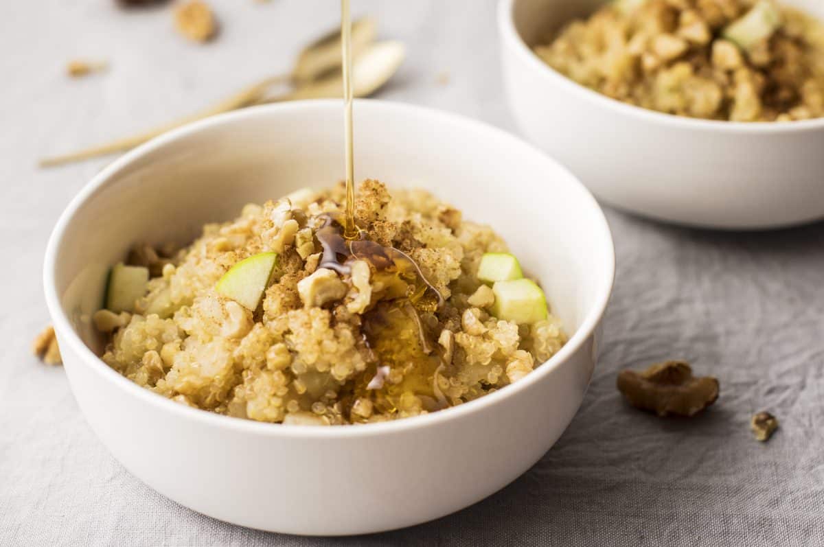 A white bowl that contains this quinoa apple breakfast recipe with a second bowl visible but blurred in the background.