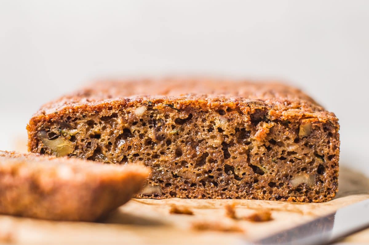 a side view of the loaf of zucchini bread on a piece of parchment paper with a slice off to the left in front