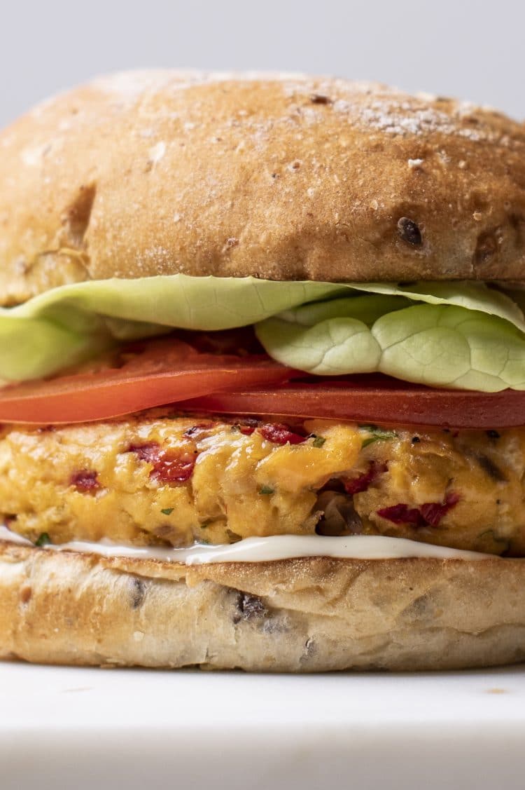 zoomed in to the side of layered sandwich with bun, mayo, salmon patty, tomato, and lettuce.