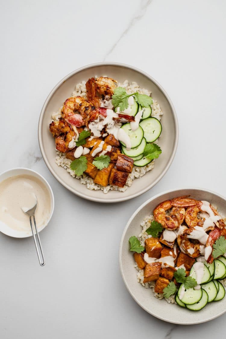 two grain bowls with a bowl of sauce on the side