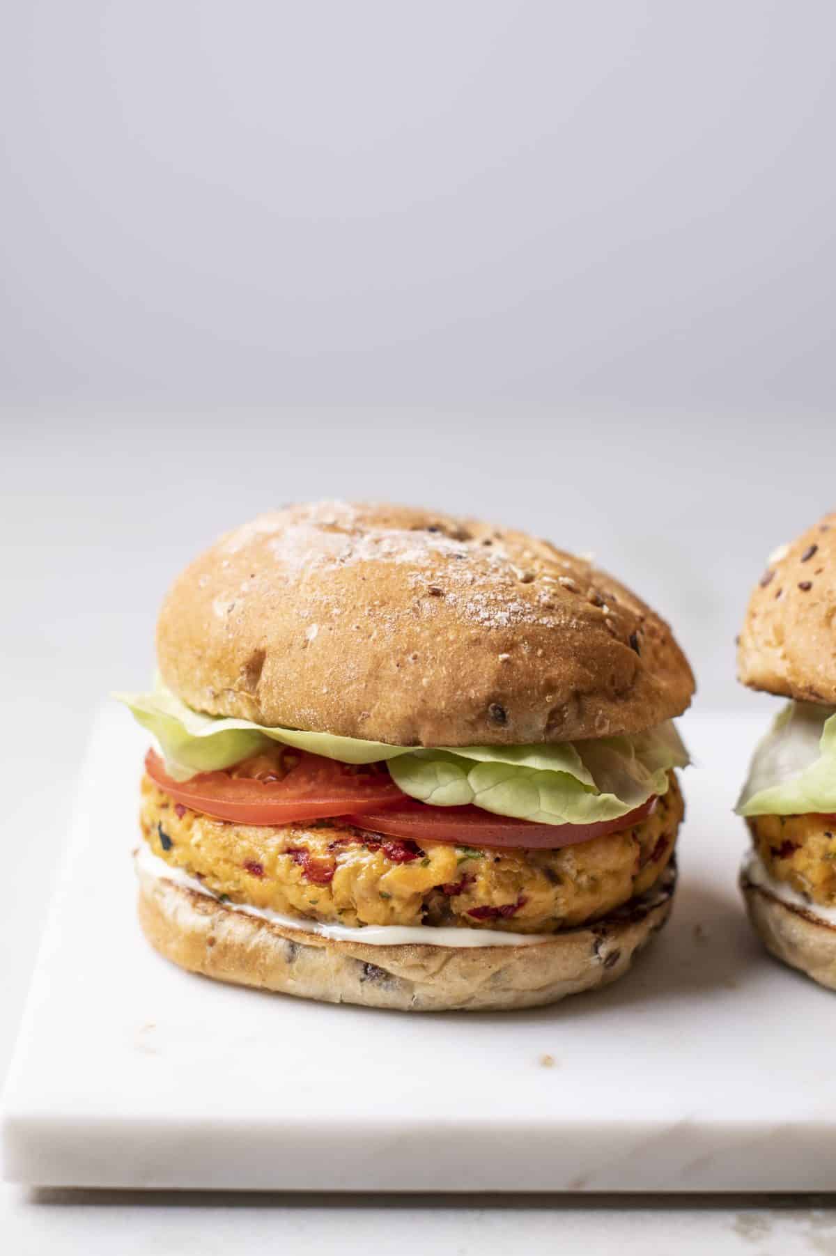 salmon burger on a white plate with another off to the right side