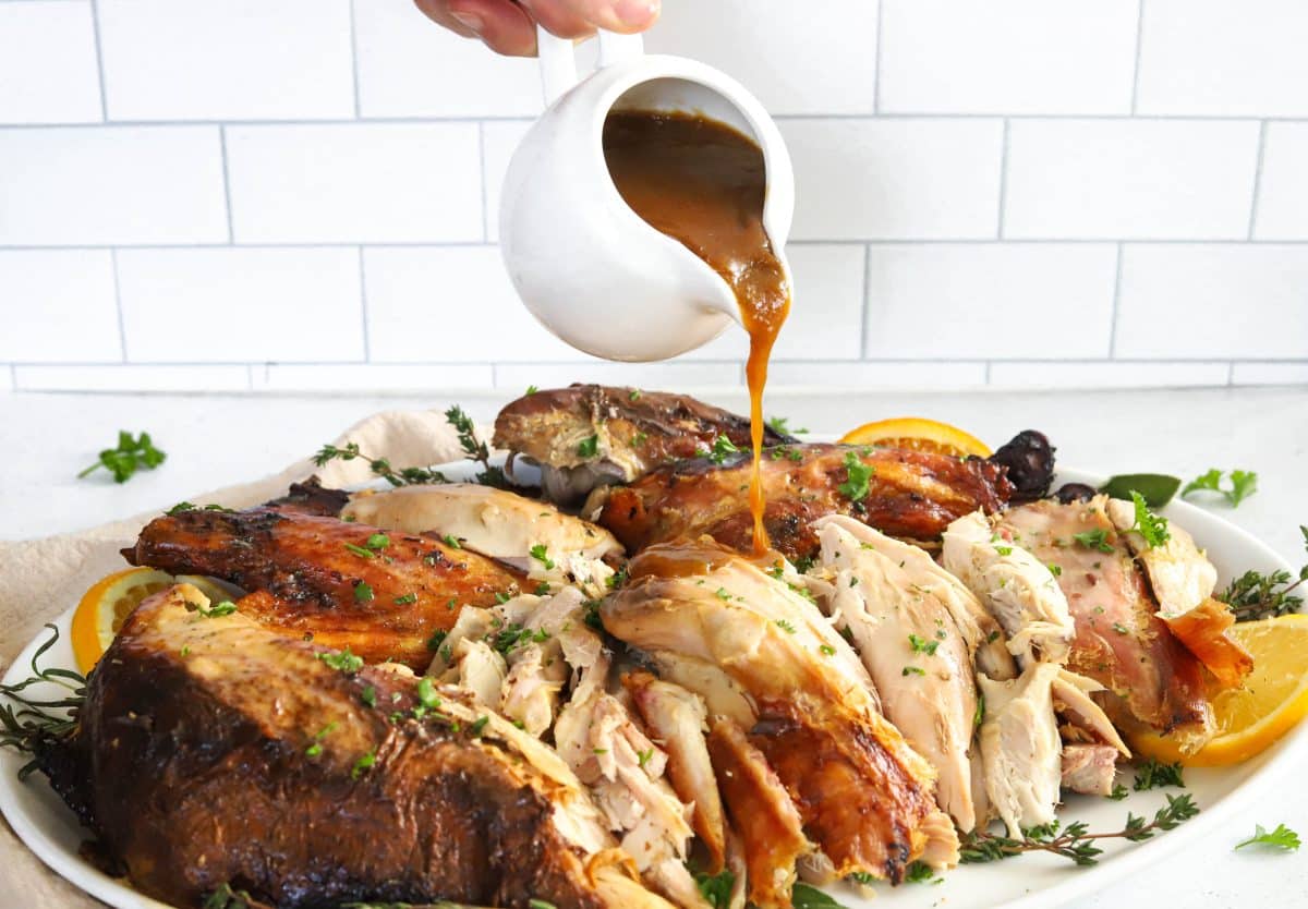 sliced turkey on a platter with a hand and gravy boat visible being drizzled on top of the turkey