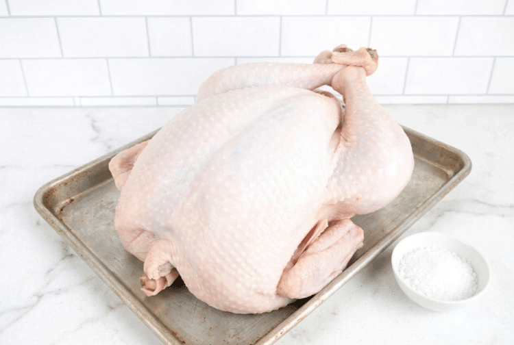 Thawed turkey on a sheet pan with a bowl of salt next to it for dry brine