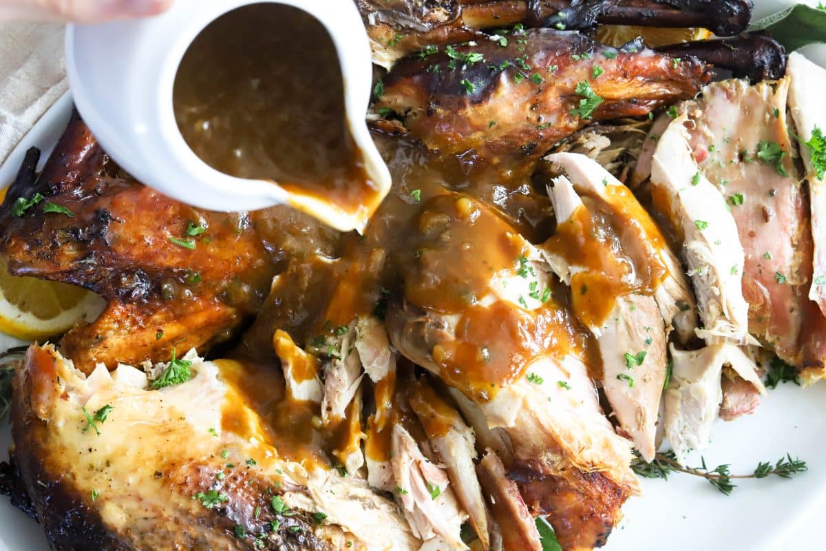 A closer view of the gravy boat pouring gravy on top of the sliced turkey