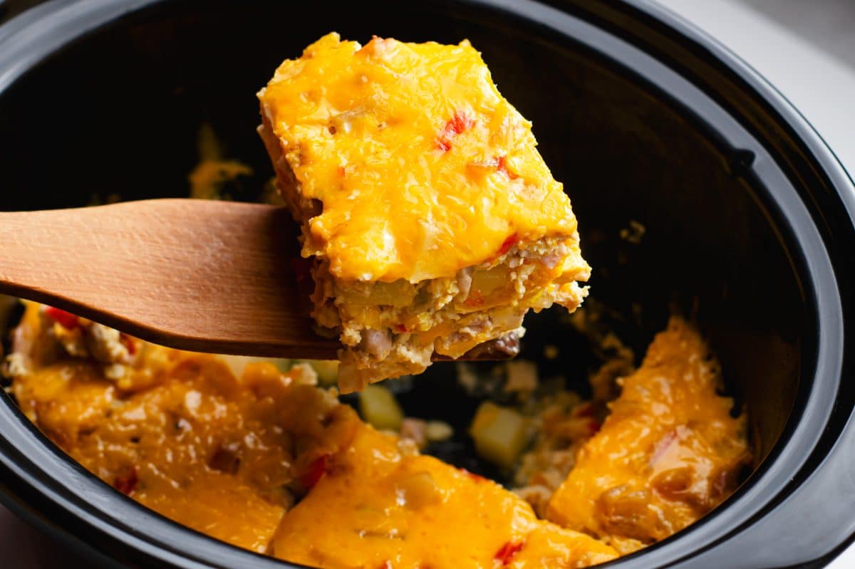 a piece of casserole on a wooden spoon over the crock pot
