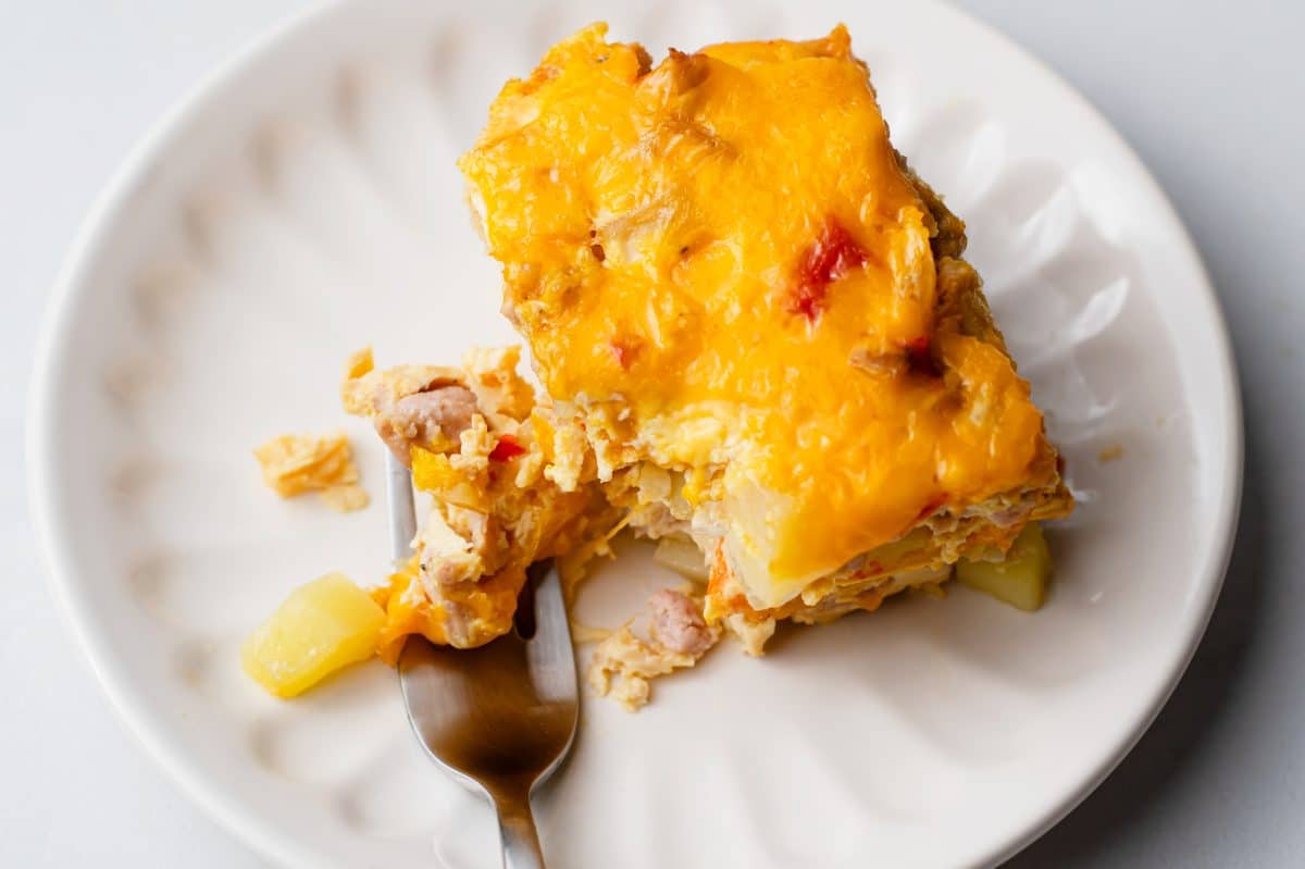 a piece of breakfast casserole on a white plate with a fork breaking it apart