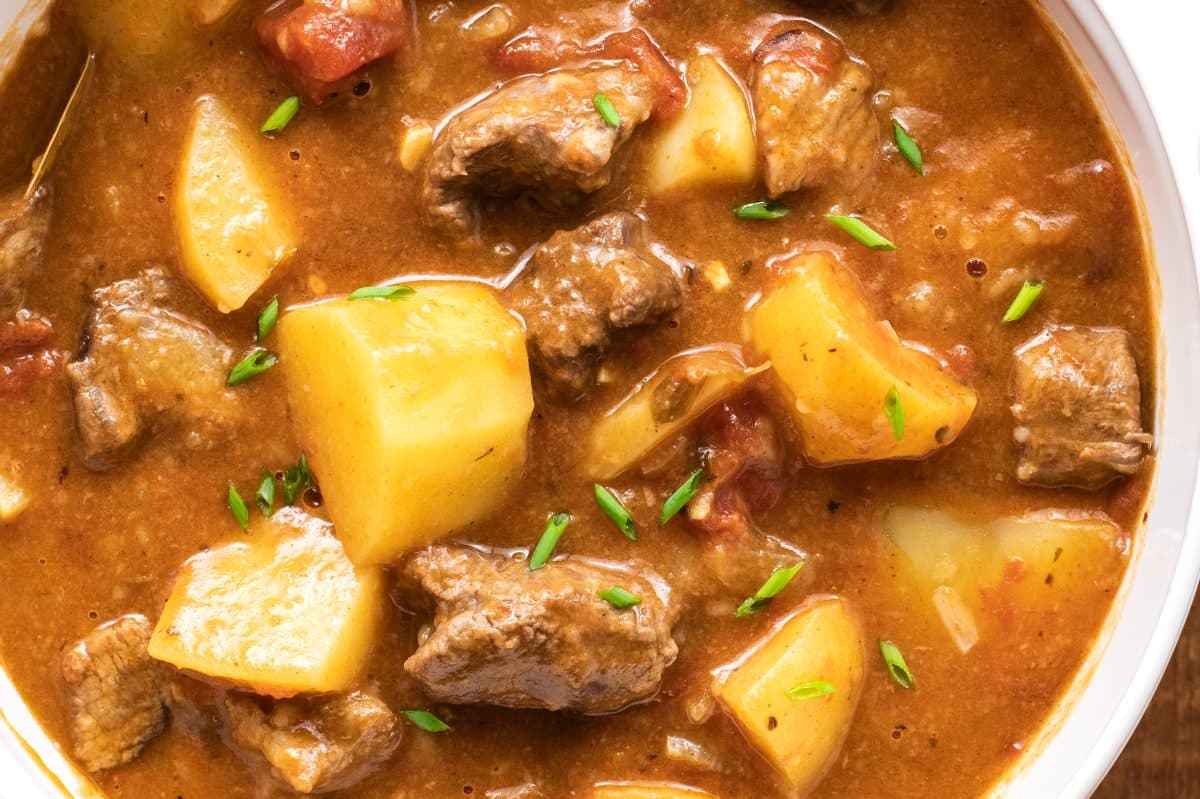 close up of hot stew in a white bowl with beef and potatoes visible below broth