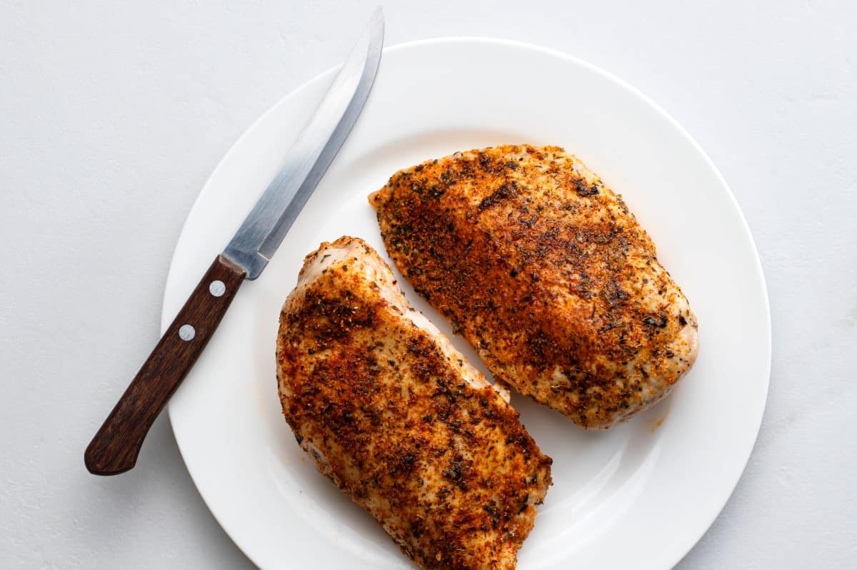 two cooked chicken breasts on a white plate with a sharp knife