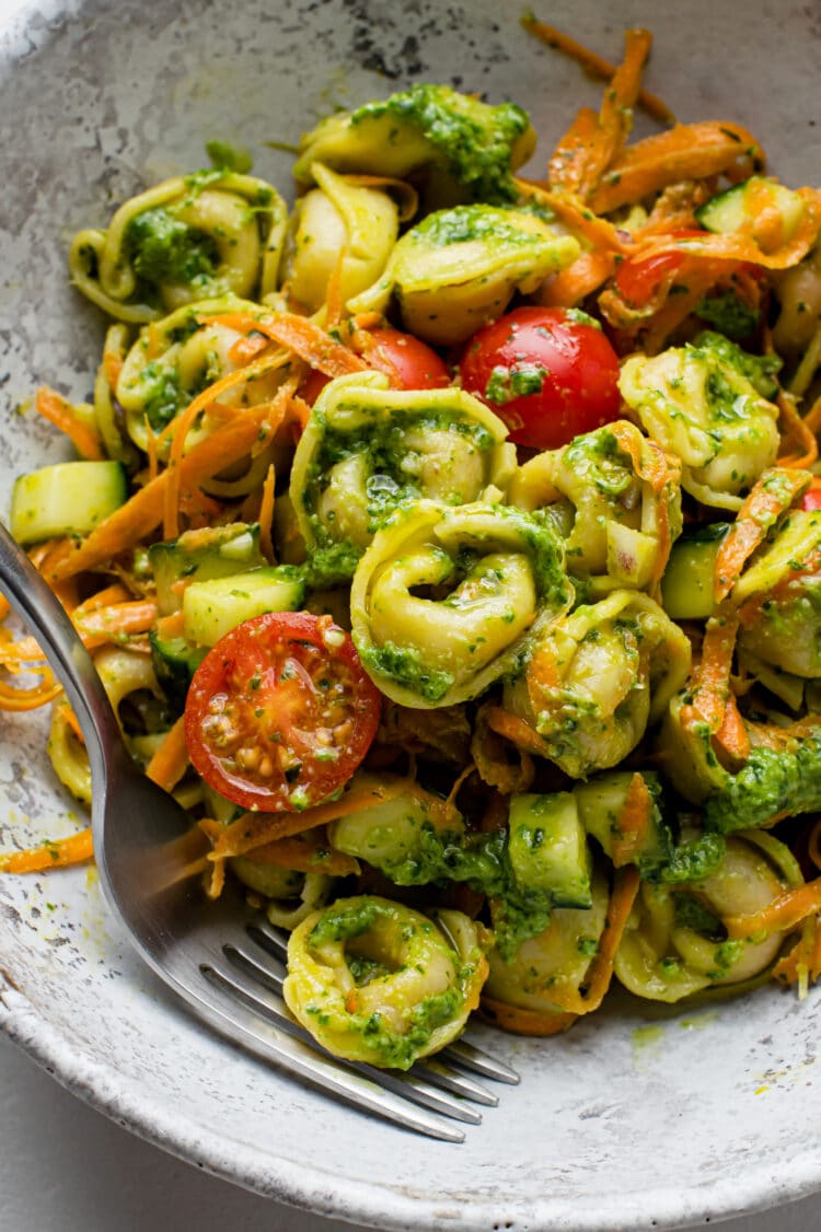 tortellini pasta salad in a light grey bowl with a fork