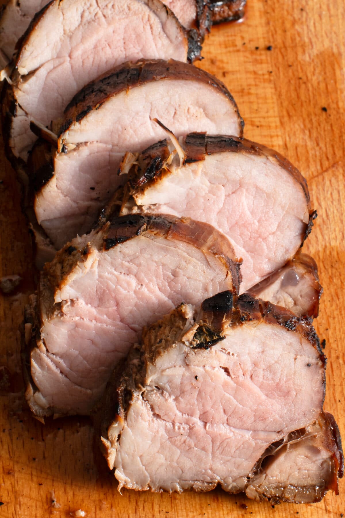 verticle image of slice tenderloin on wooden cutting board