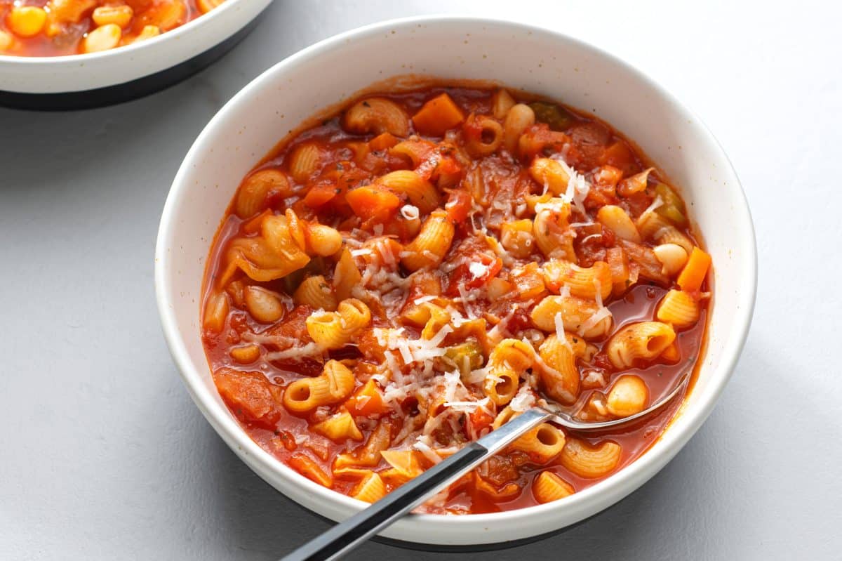 minestrone soup in a white bowl with a silver spoon