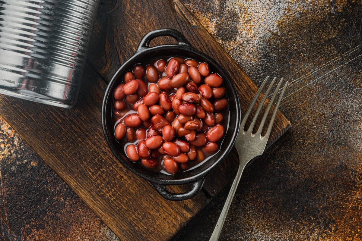 A black bowl of red beans with a fork over a wooden cutting board,