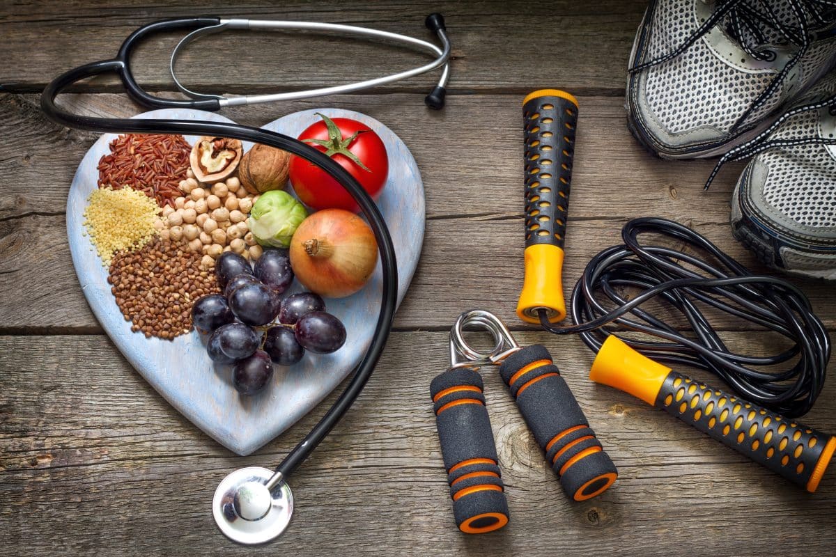 A heart-shaped plate of food next to a stethoscope, workout equipment, and gym sneakers.
