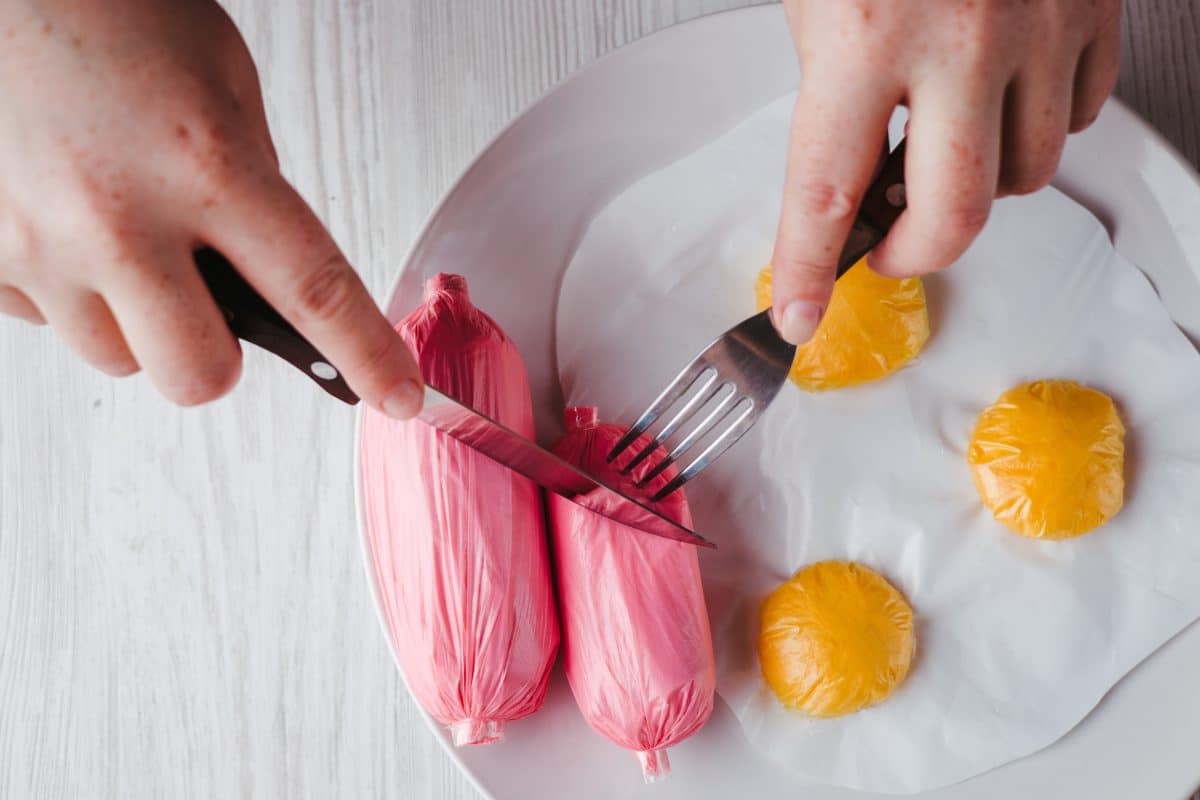Cutting into plastic sausages and eggs on a plate. 